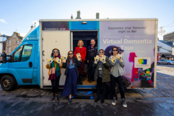 Dementia-Experience-Bus-Maggie-Ellis-and-Group-Outside-with-hands-up-A97A4725-low-res