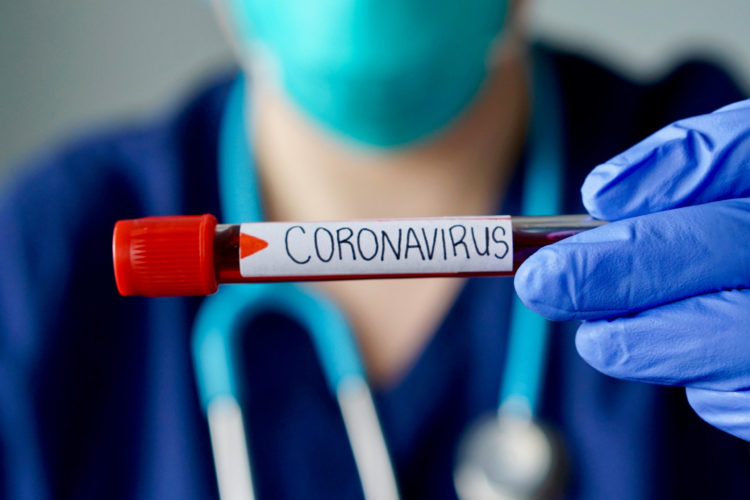 Masked medical professional holds a blood vial with 'coronavirus' written on in