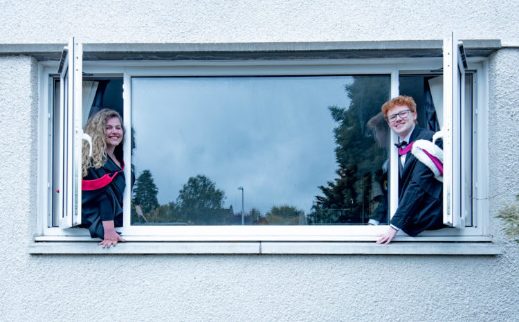 Students in graduating robes sit on a window ledge
