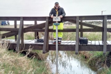 Man standing on bridge dropping pole into water