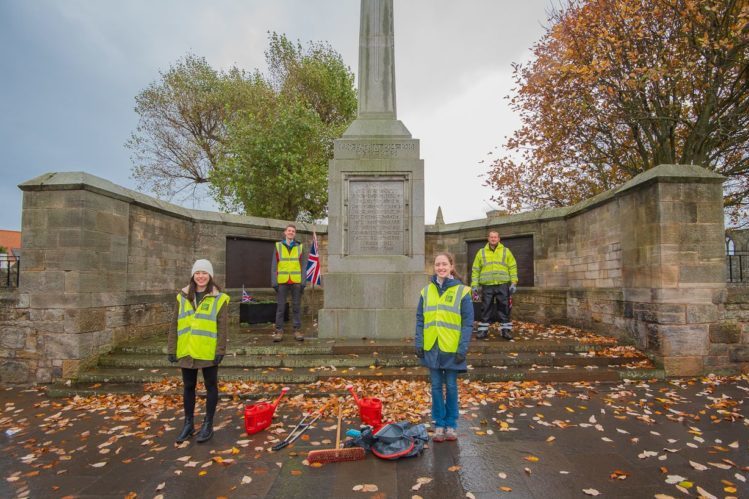 Students in hi-vis vests picking up litter around a monument