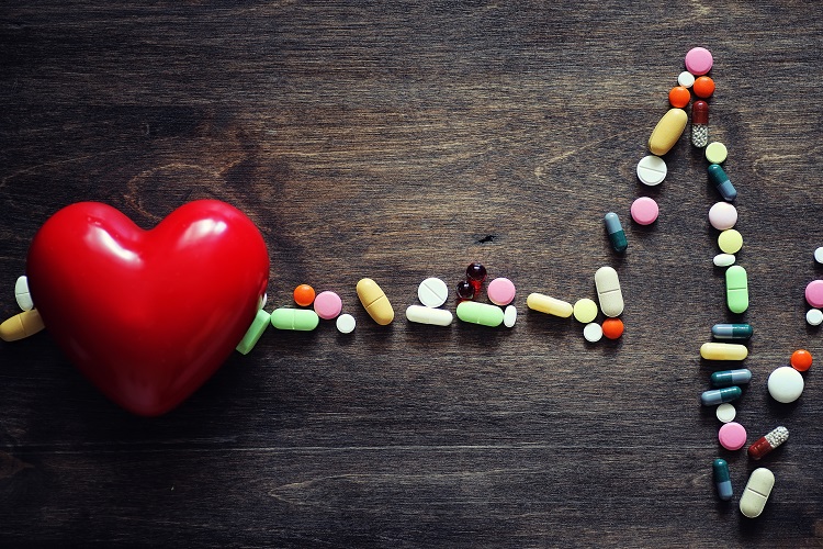 The concept of heart health dependence on tablets. Pills and stethoscope on wooden background.