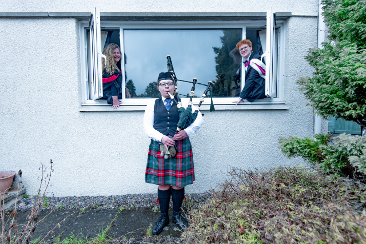 Two graduating students leaning out of their window listening to a piper playing