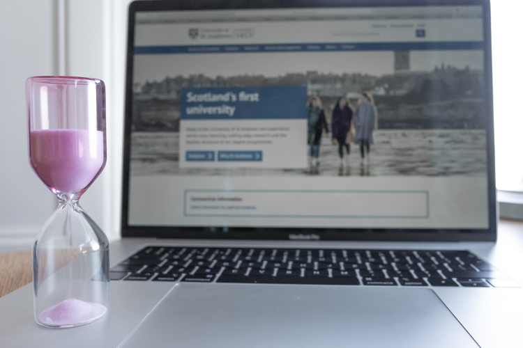 Laptop showing the University homepage with a pink sand timer in front of it