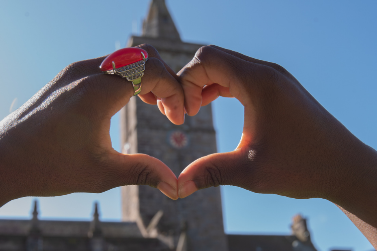Two hands together forming a love heart sign in front of St Salvator clock tower