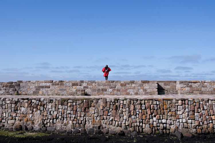 Student standing alone in the middle of St Andrews pier wearing a red academic gown