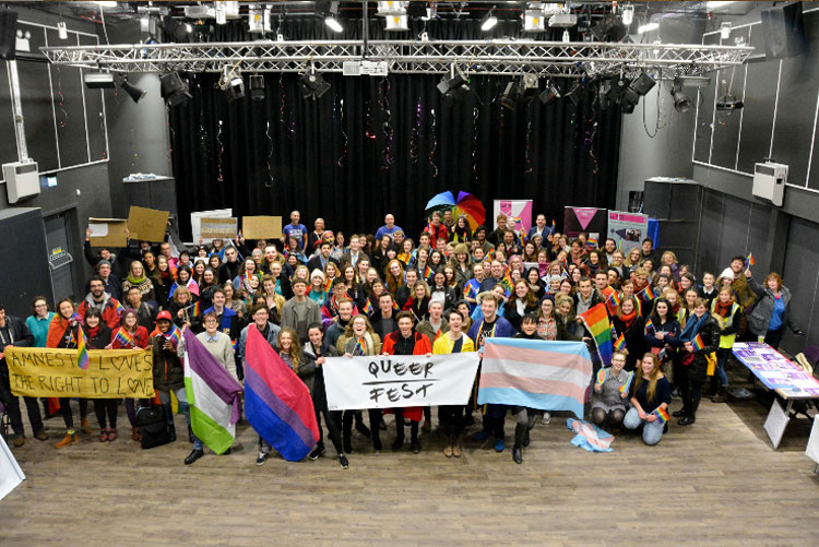 A group of students hold various banners for Queer Fest