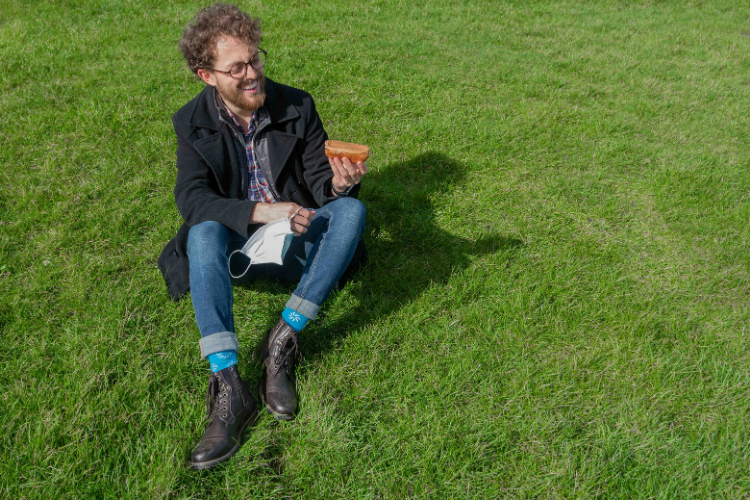 Male student sitting on the grass with a fudge doughnut in his left hand