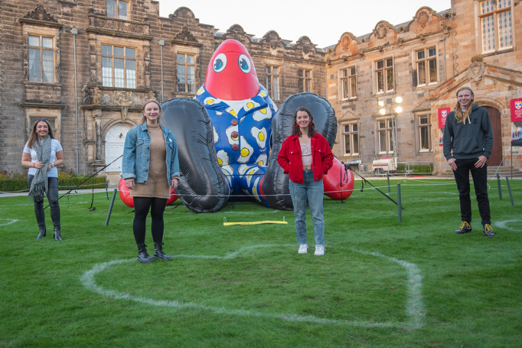 Four students standing socially distant in front of a giant inflatable lobster