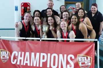 Saints Women's Water Polo team standing in front of a banner that reads BUCS Champions