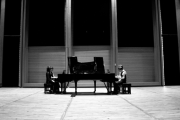 Four pianists sit at pianos in the University's Music Centre. Image is black and white.