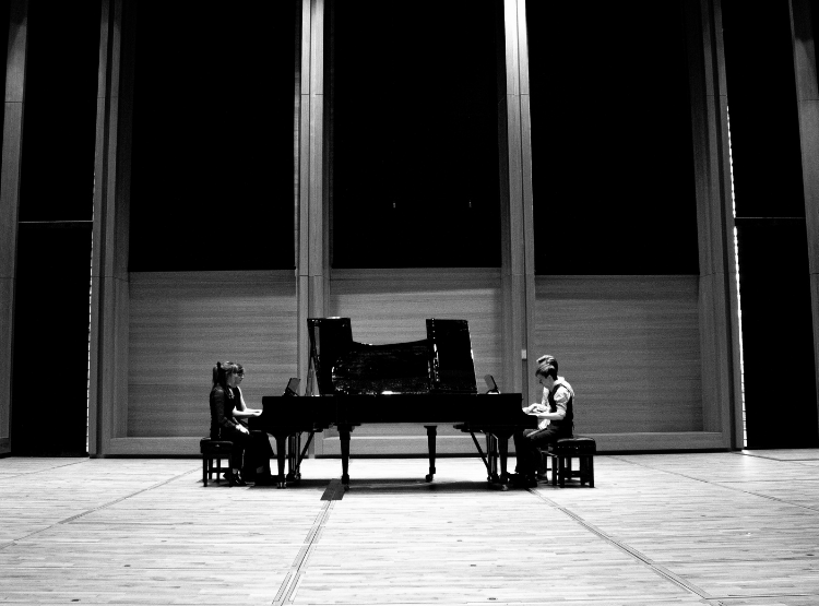 Four pianists sit at pianos in the University's Music Centre. Image is black and white.