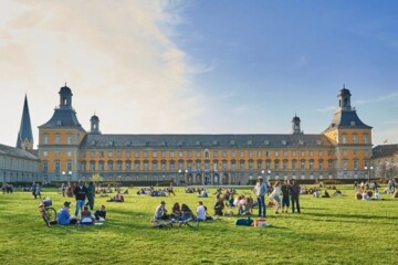 Students sitting and standing on grass outside University of Bonn buildings