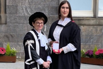 two people standing with academic regalia holding a medal