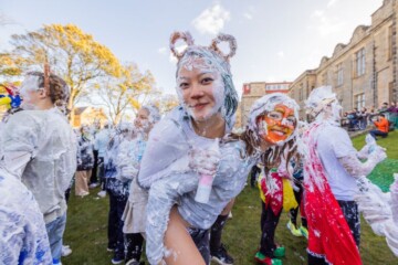 Students in fancy dress covered in shaving foam posing for the camera on Lower College Lawn