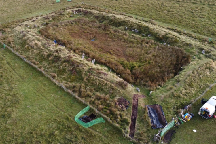 A rectangular mound is visible in grass, with standing stones surrounding it