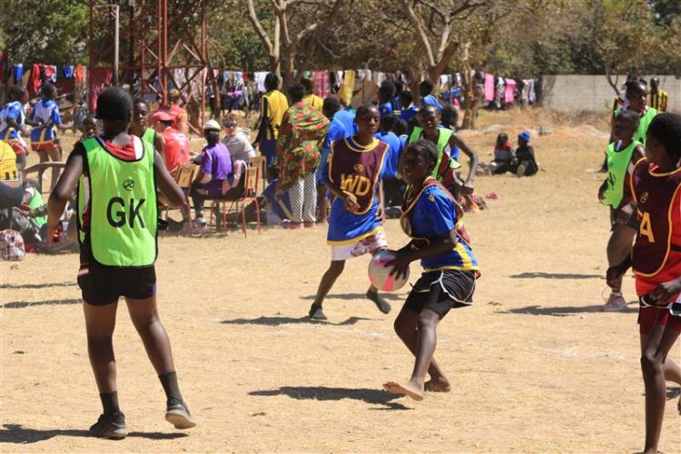Children playing netball wearing sports vests and with people watching on