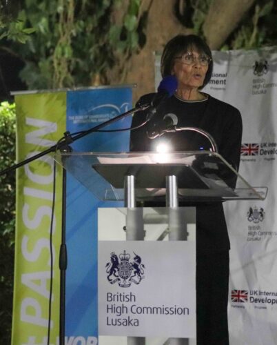 A woman stands at a podium giving a speech and the podium sign reads 'British High Commission Lusaka'