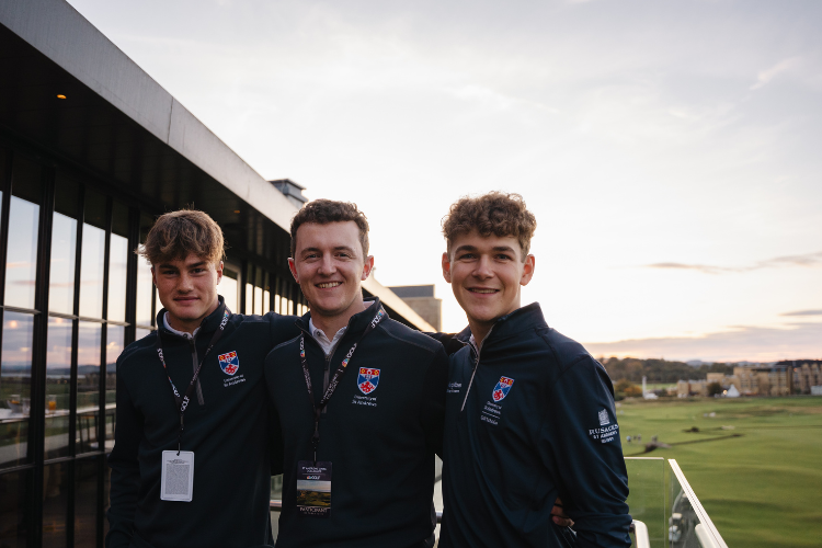 three smiling golfers on a rooftop terrace with the old course behind them