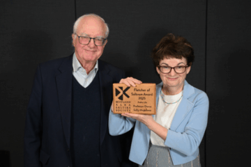 A woman is presented with an award by a man, both smiling