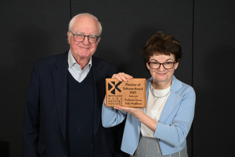 A woman is presented with an award by a man, both smiling 