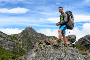 A man with a backpack stands on top of a rock